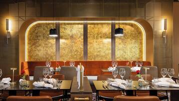 A restaurant with a modern interior, featuring a long table with multiple chairs, a decorative wall with a textured pattern, and pendant lighting.