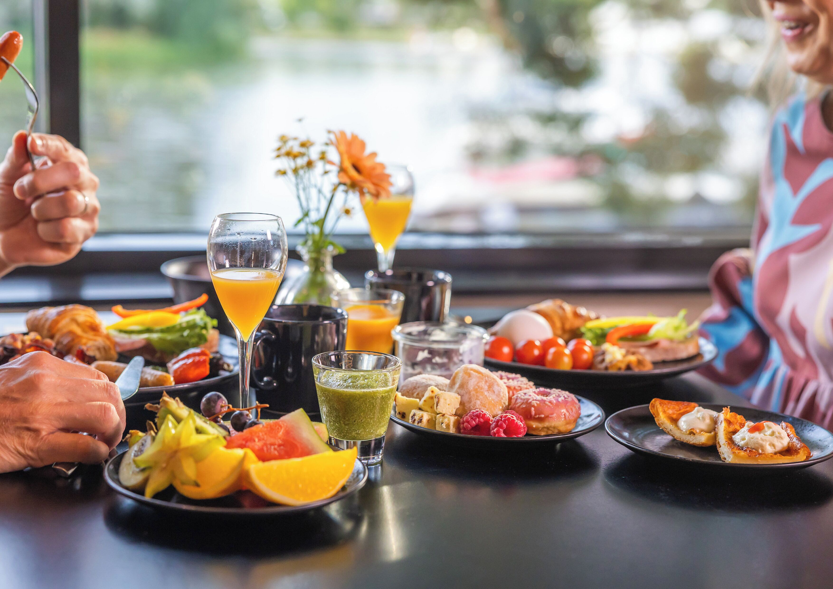 A dining table with various dishes, drinks, and a vase of flowers.