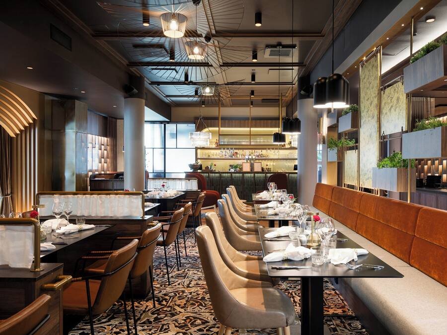 A restaurant with a long dining table, multiple chairs, and a bar area in the background.