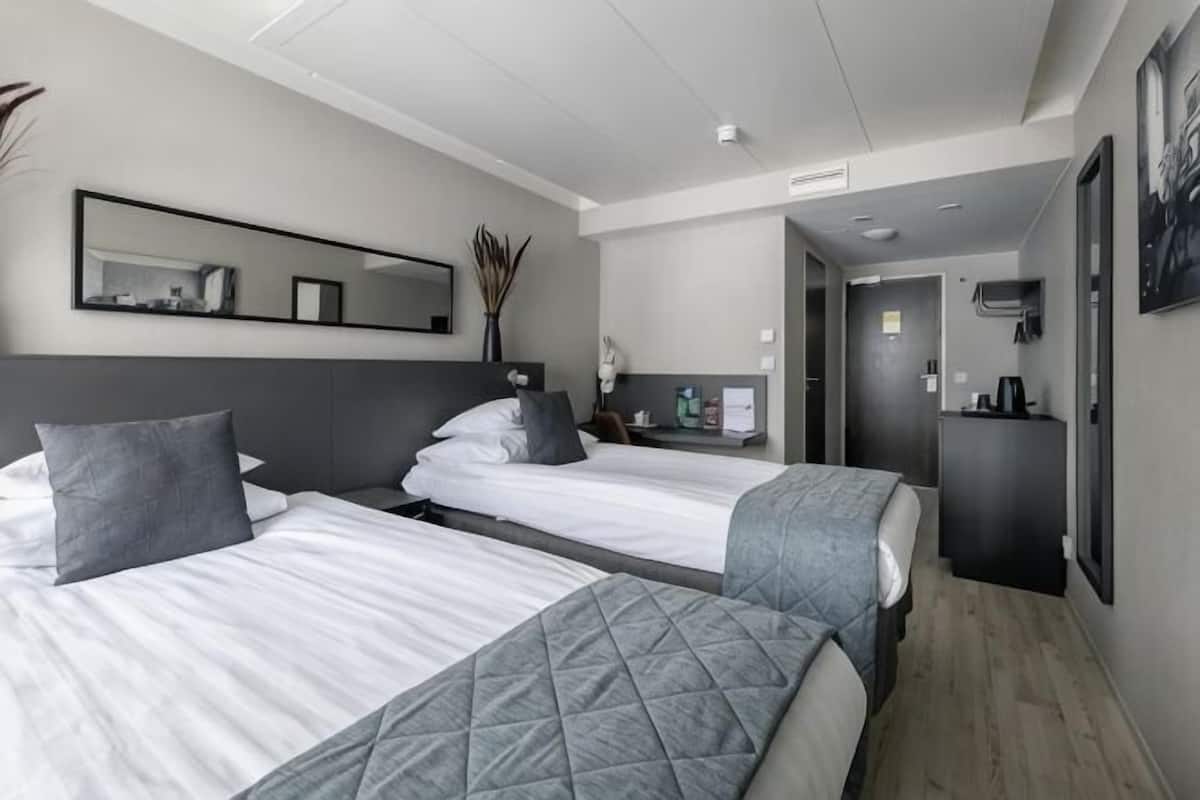 Ein Hotelzimmer mit zwei Betten, einem Spiegel, einem Schreibtisch und einem durchgegangenen Badezimmer.