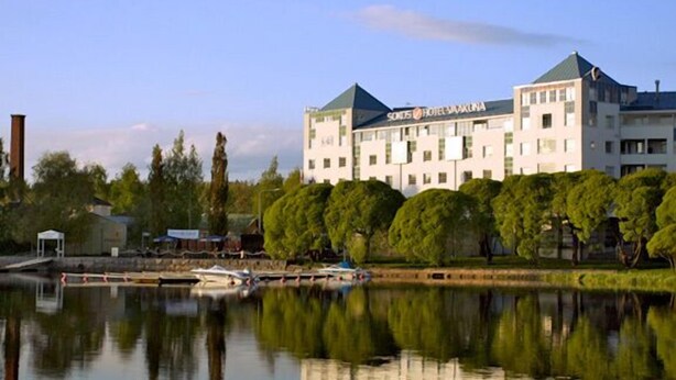 Un hôtel doté d’un grand bâtiment, situé en bordure d’une étendue d’eau et entouré d’arbres.
