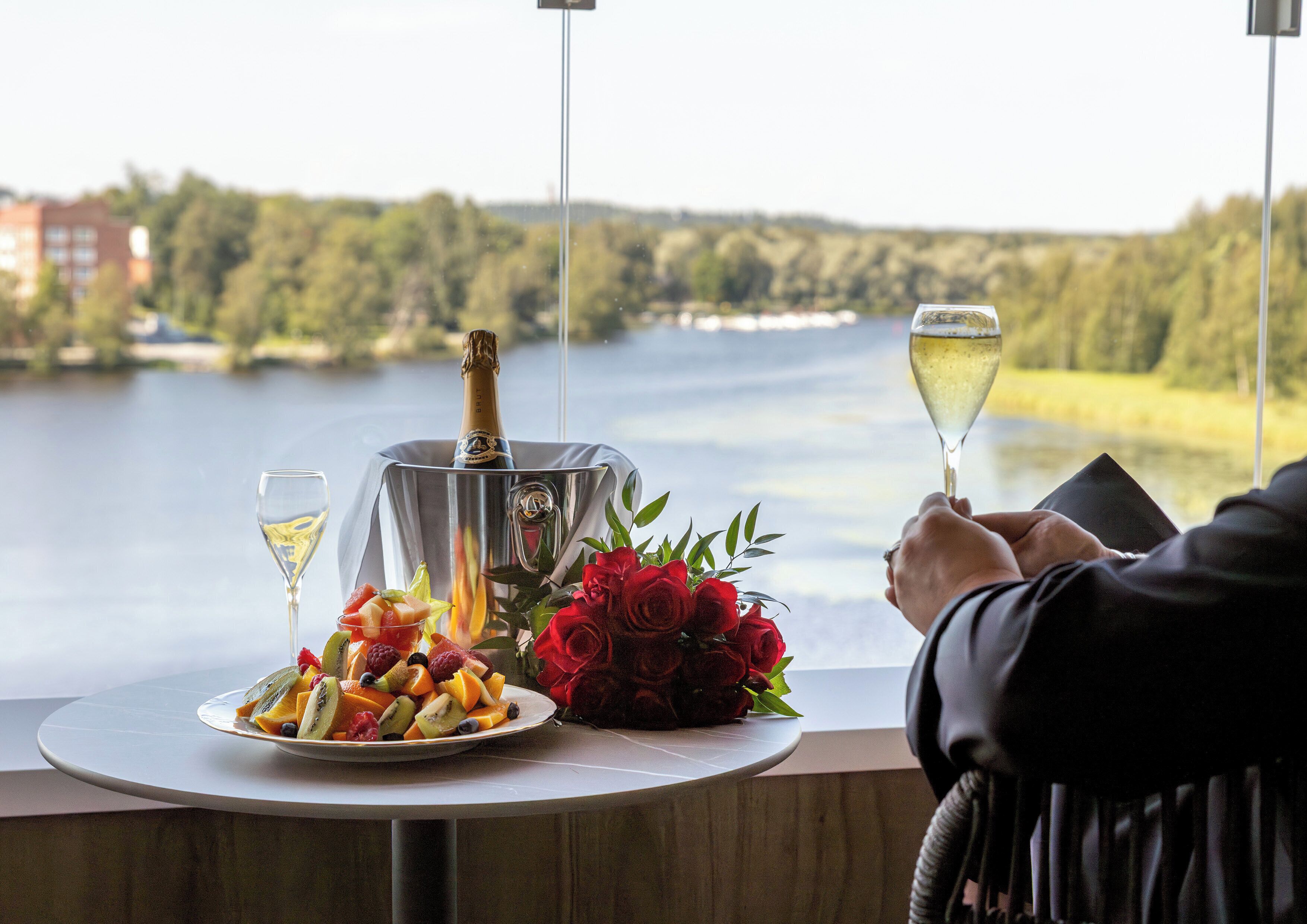 Ein Tisch mit einer Champagnerflasche, einem Weinglas, einer Obstplatte und einem Strauß roter Rosen.
