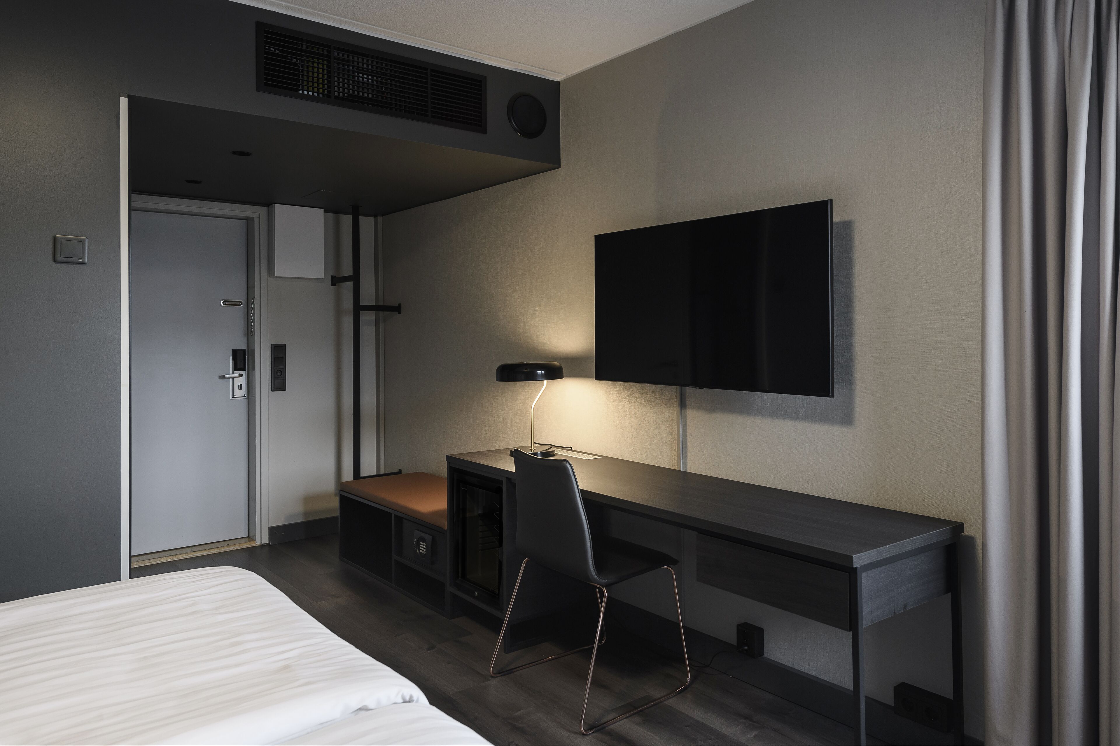 Una habitación de hotel moderna con cama, escritorio, silla, televisor y armario.