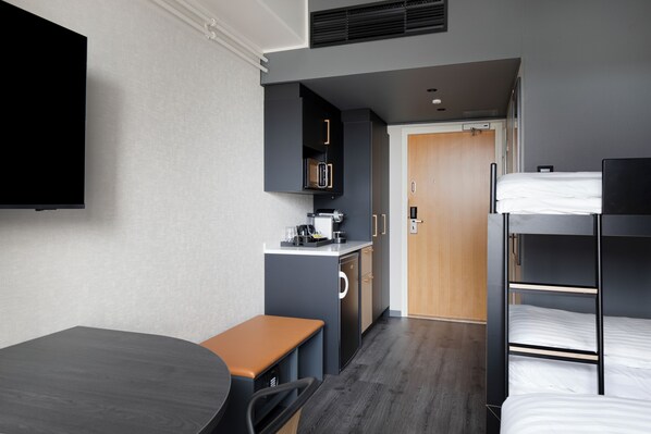 Una habitación de hotel compacta con kitchenette, una cama individual, un escritorio y televisión.