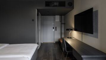 Una habitación de hotel moderna con una cama, un escritorio con una silla, un televisor de pantalla plana montado en la pared y una puerta que da al baño.
