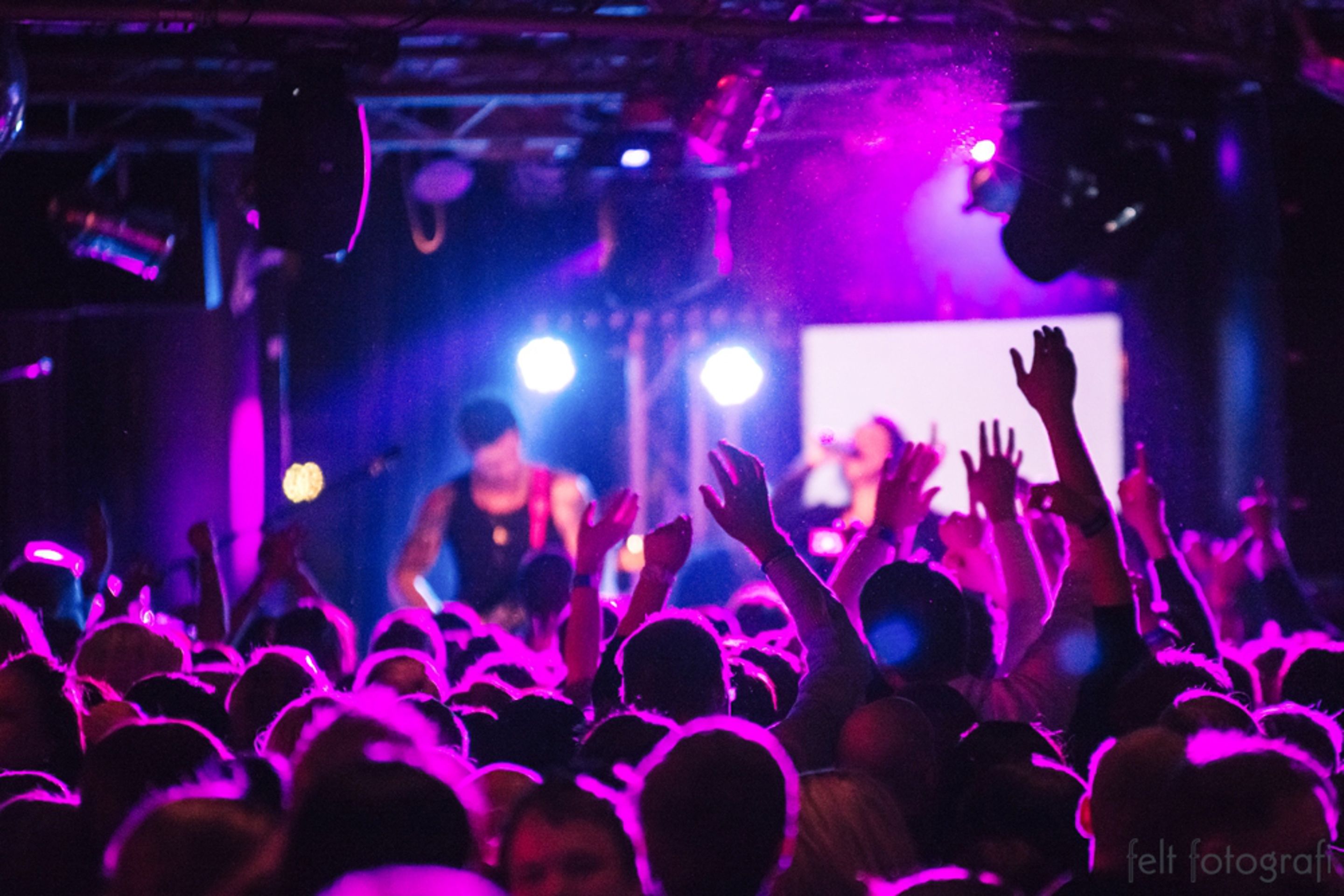 A crowded indoor event with people raising their hands, possibly at a concert or gathering.