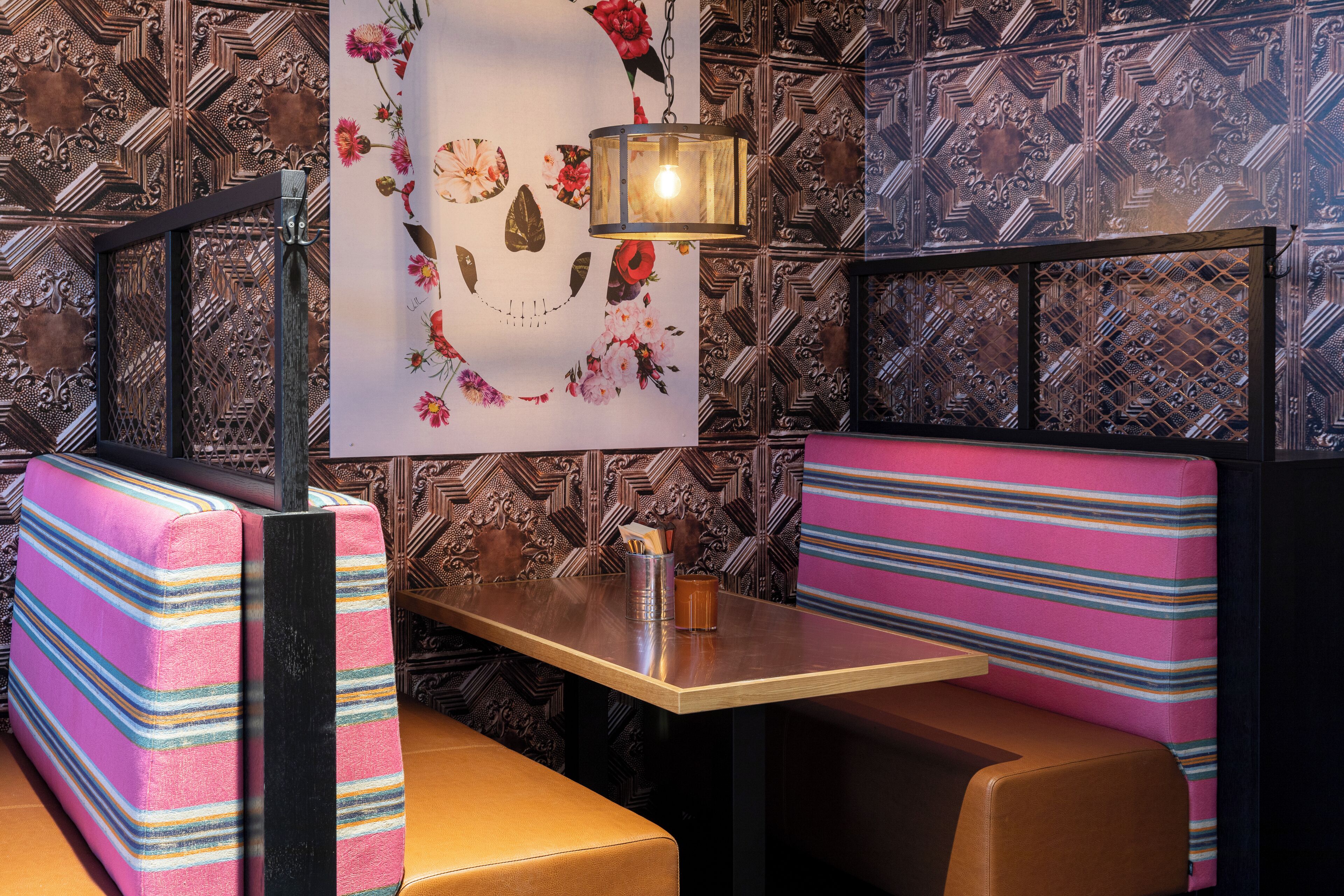 A restaurant interior with patterned wallpaper, a table with a lamp, and striped booth seating.