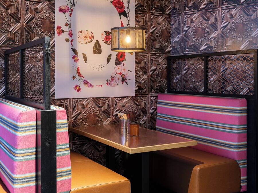 Interior de restaurante con papel tapiz estampado, una mesa con lámpara y asientos tipo cabina a rayas.