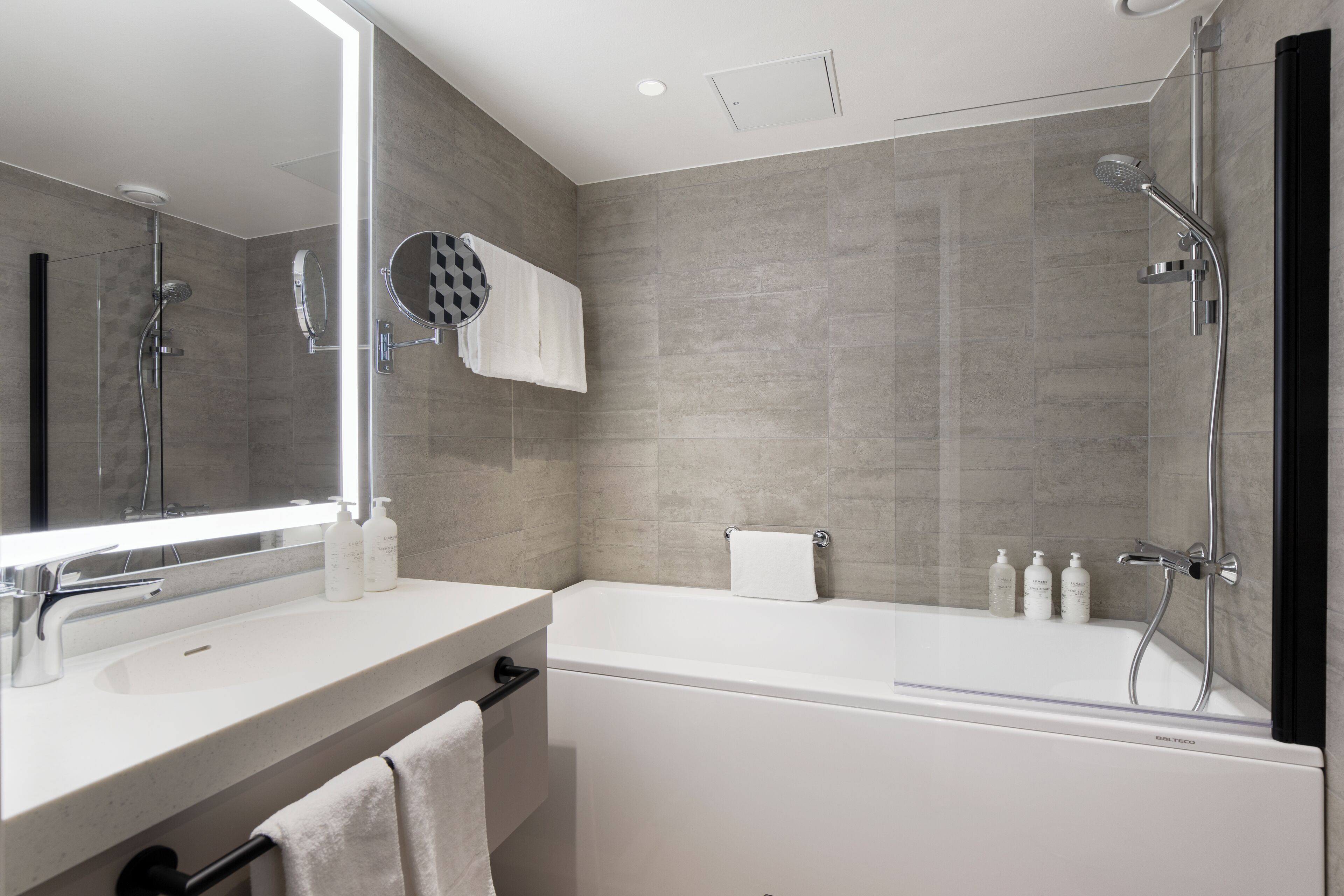 A modern bathroom with a large mirror, a bathtub, and a shower area.