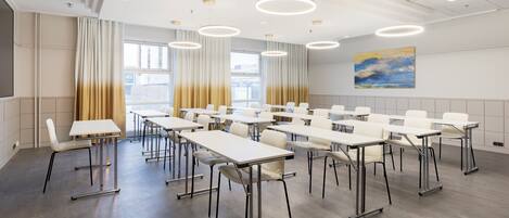A conference room with white tables and chairs, large windows with curtains, and a painting on the wall.