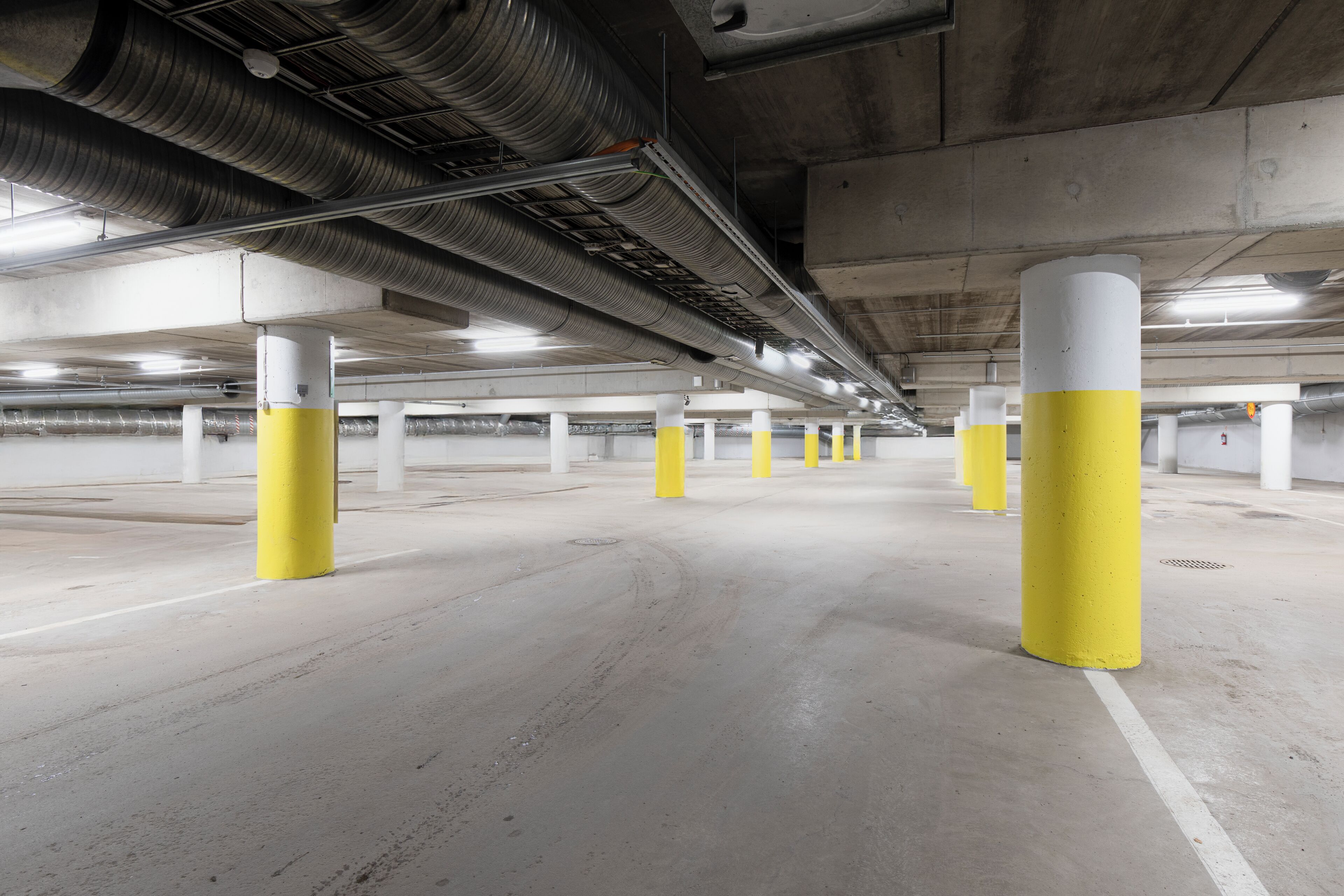 An underground parking garage with concrete pillars and ventilation ducts.