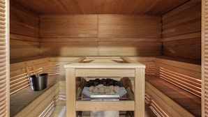 A sauna with wooden walls and a shelf holding a metal container and a tray of stones. - Original Sokos Hotel Vantaa (Vantaa)