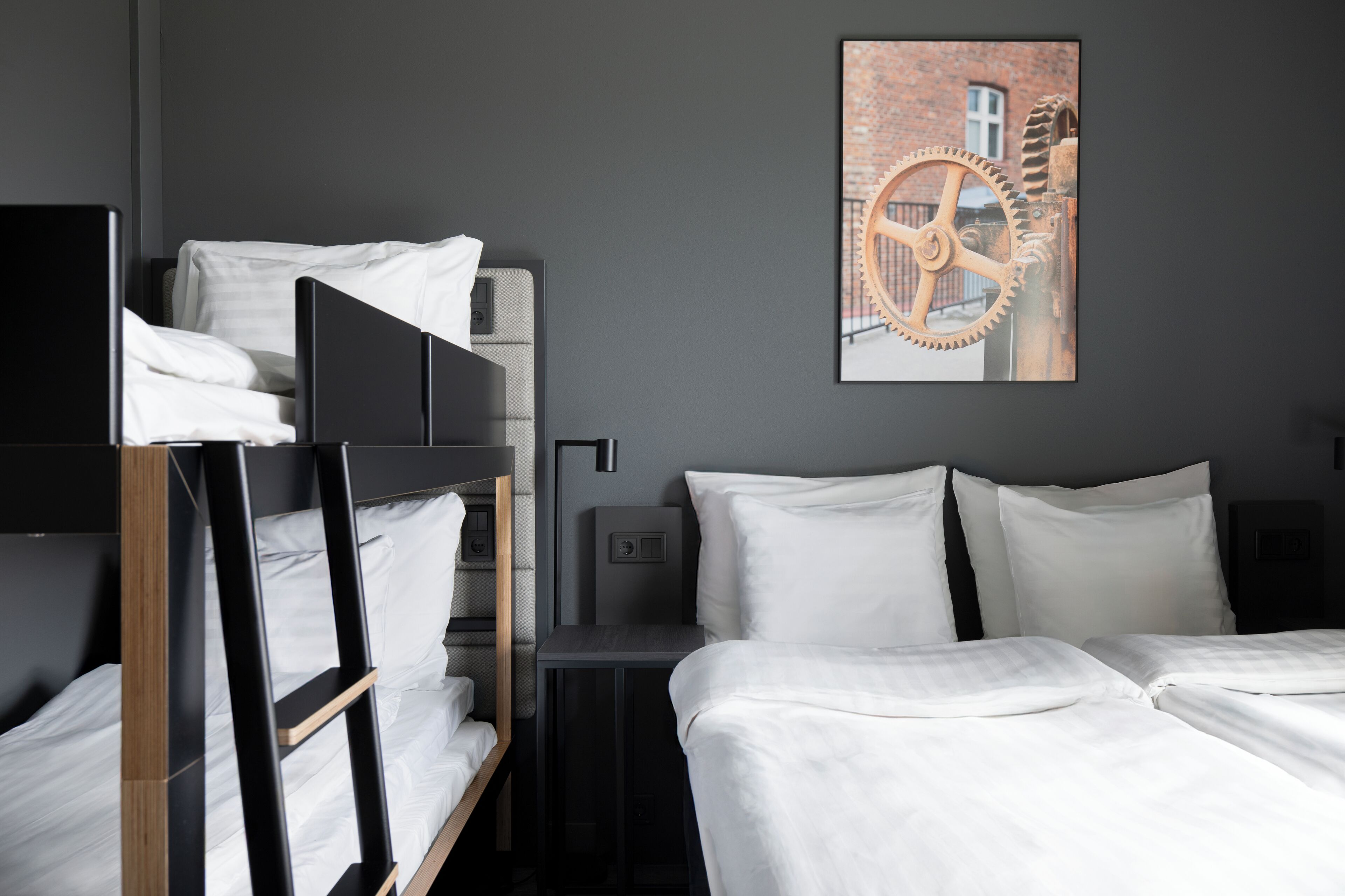 Habitación de hotel con literas, un escritorio, una silla y un cuadro de un engranaje en la pared.
