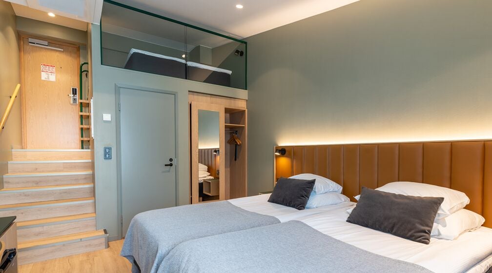 A hotel room with a bed, a wardrobe, a mirror, and a staircase.