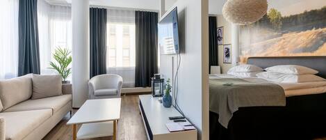 A modern hotel room with a bed, a sofa, a desk, and a TV.