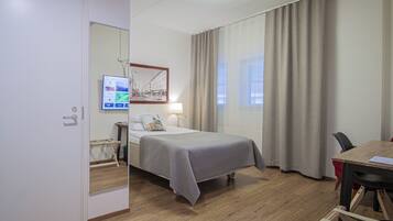 A hotel room with a bed, a desk, a chair, a lamp, and a window with curtains.