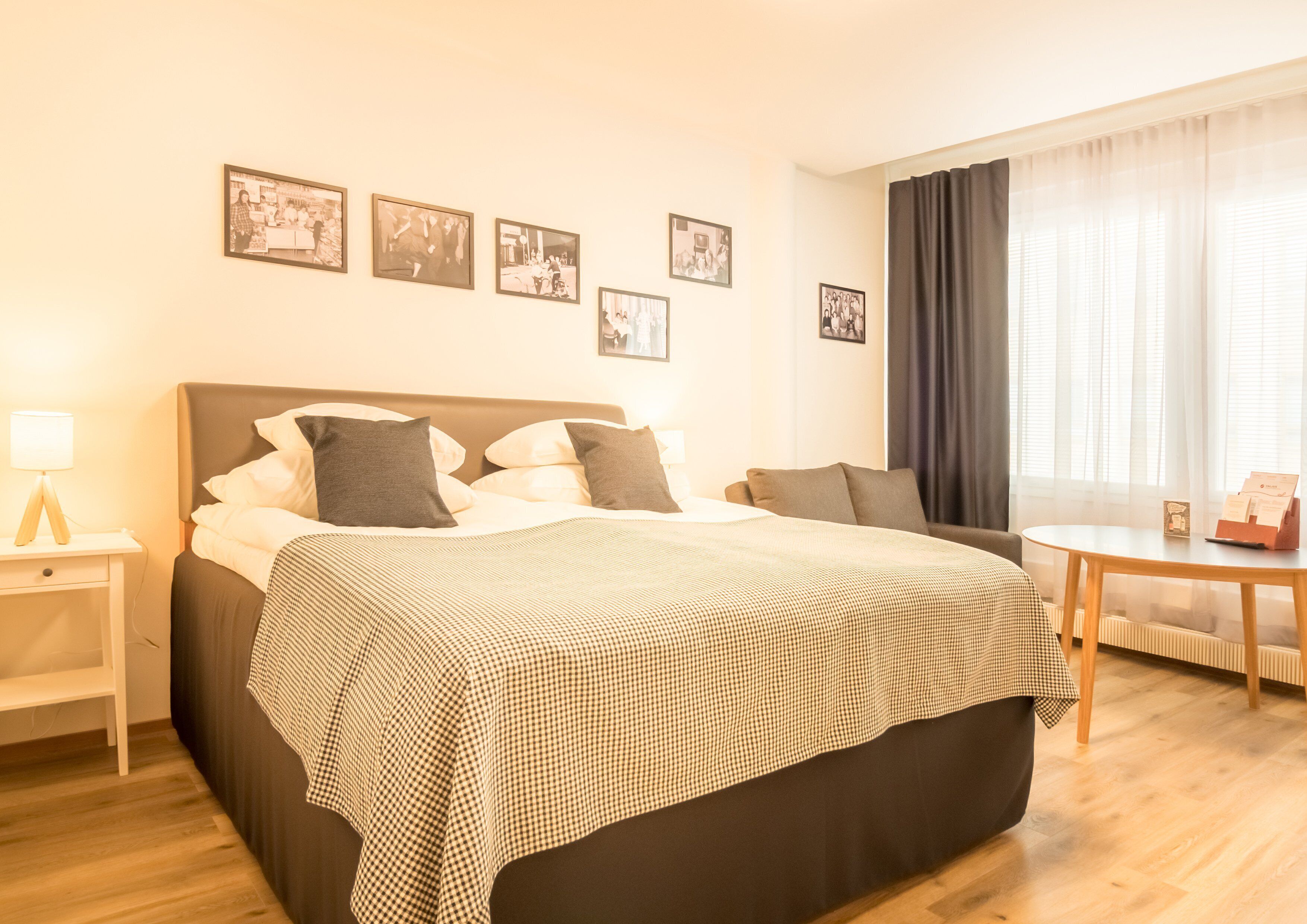 Et hotelværelse med seng, natbord, lampe og et lille bord med holder til kort.