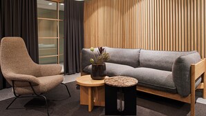 Una sala de estar moderna con un sofá gris, un sillón marrón, una mesita de madera y una pequeña mesa redonda con un florero de flores secas.
