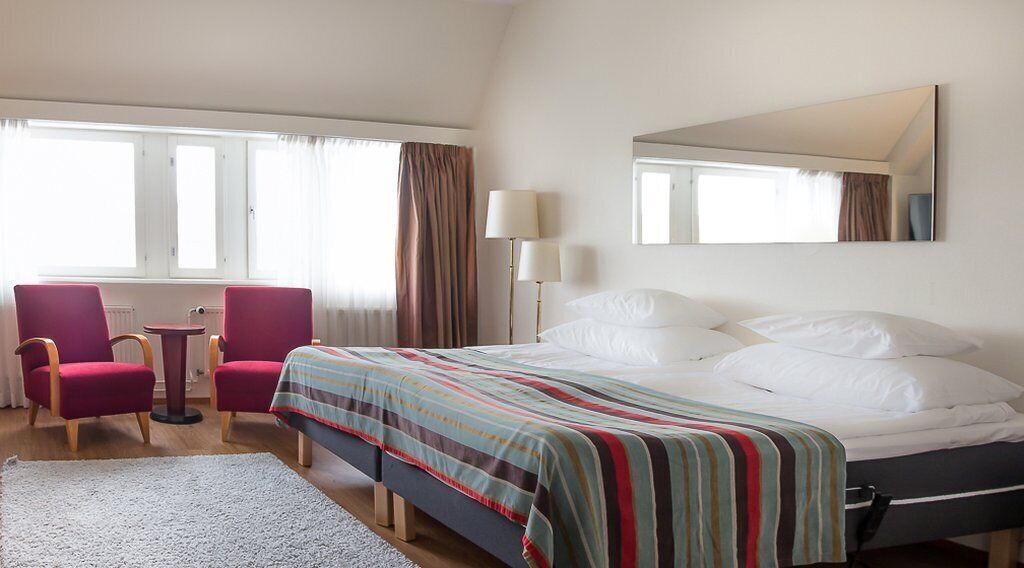 Habitación de hotel con cama, escritorio, dos sillas, lámpara y un espejo grande.