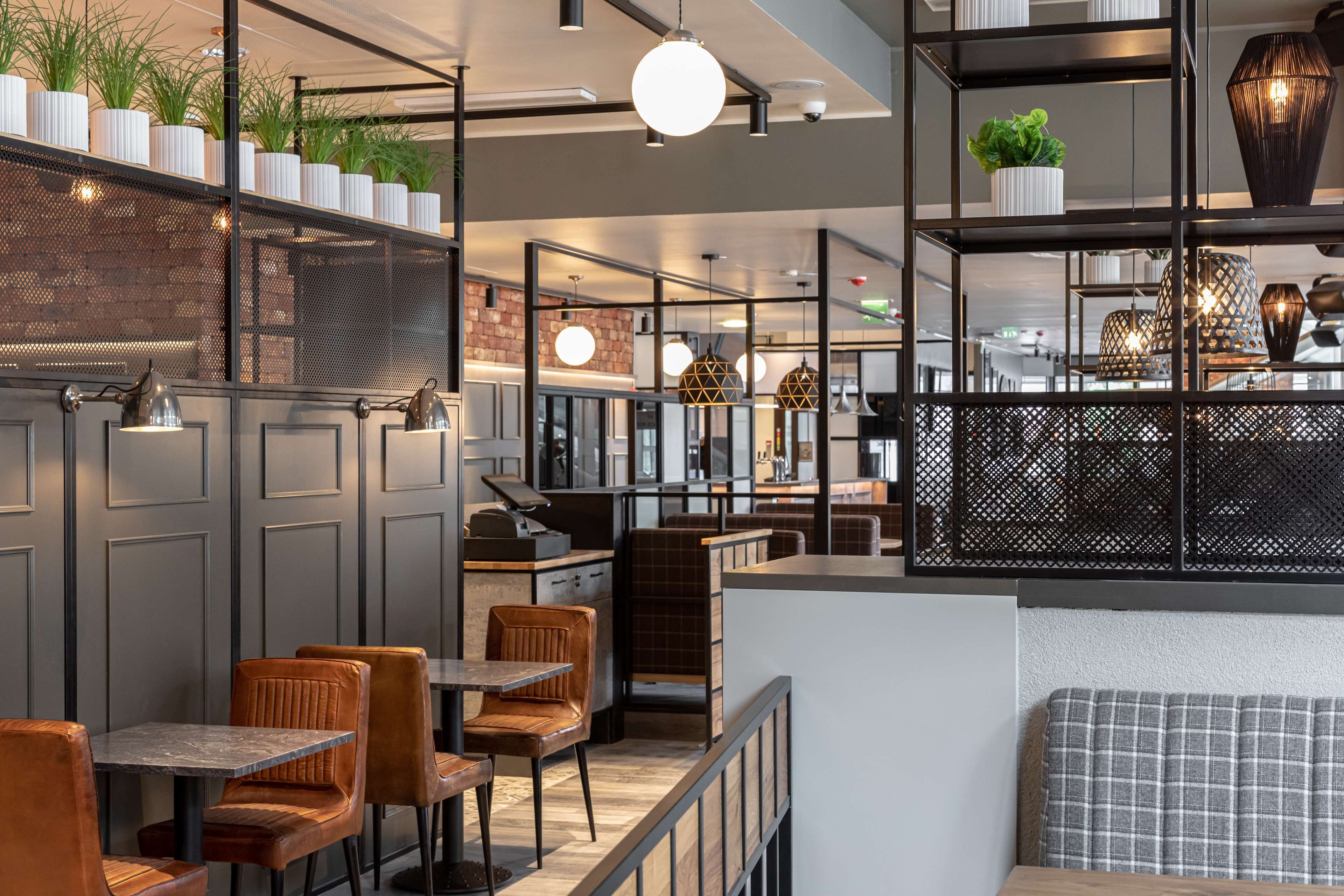 En modern restauranginteriör med höga bord, bekväma stolar och dekorativ belysning.