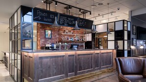 A modern bar area with a wooden counter, hanging lights, and a menu board. - Scandic Pasila (Helsinki)