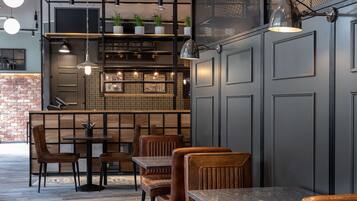 Interior de restaurante con suelo de madera, asientos de cuero, una zona de bar con estanterías e iluminación colgante.