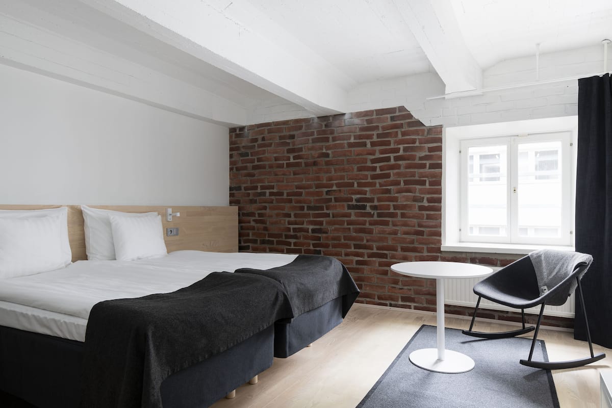 Habitación de hotel con una cama grande, una mesita redonda pequeña, un sillón mecedor y una pared de ladrillo.