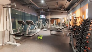 Un gimnasio con cintas de correr, máquinas de pesas y un estante con mancuernas.
