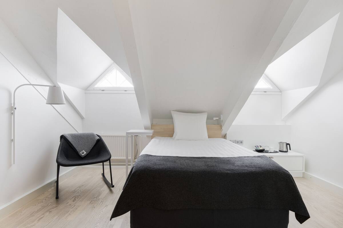 Un dormitorio moderno y minimalista con una cama, una silla y una mesita de noche.