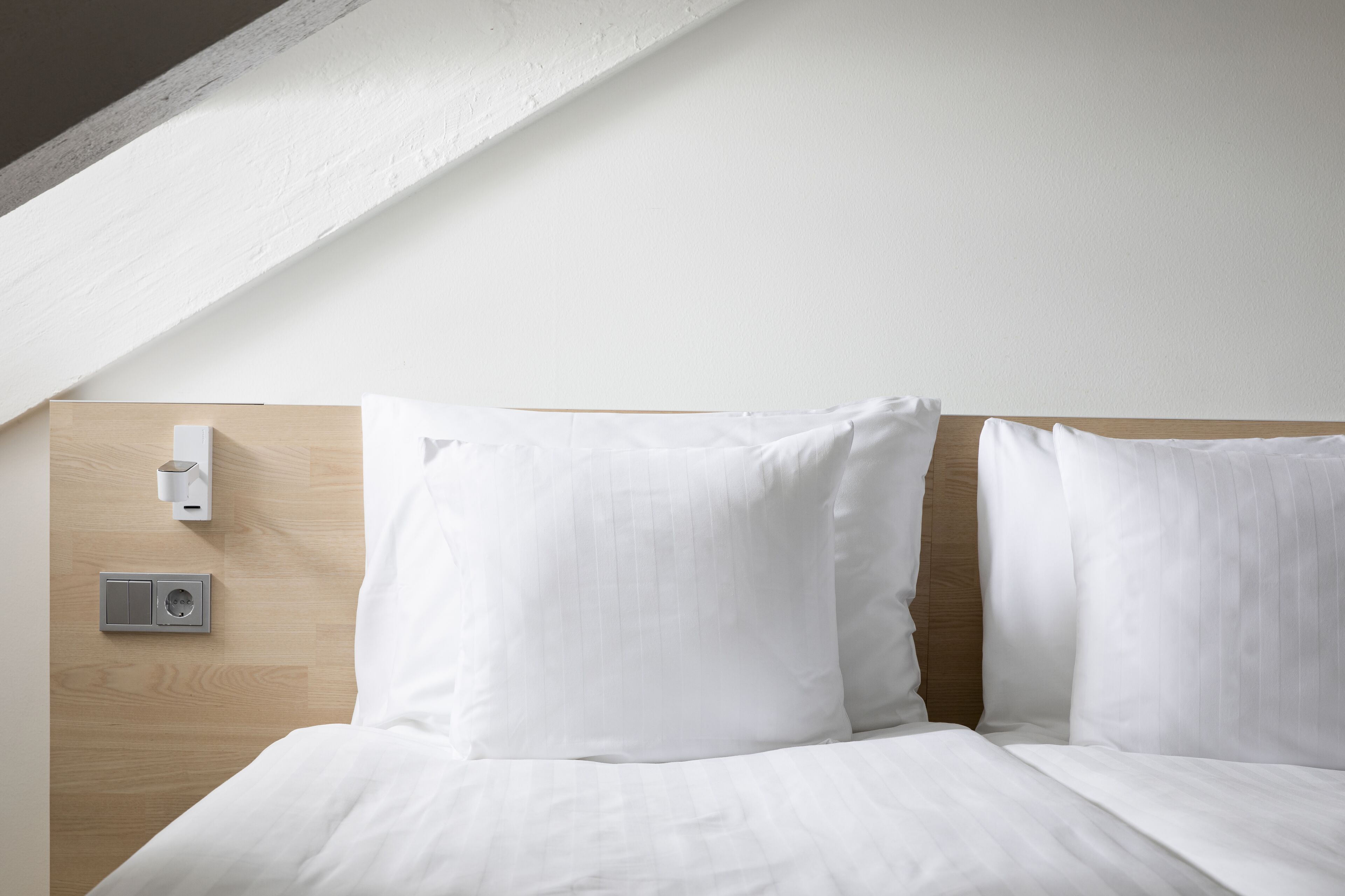Una cama bien hecha con sábanas blancas, cabecera de madera y panel de control en la pared.