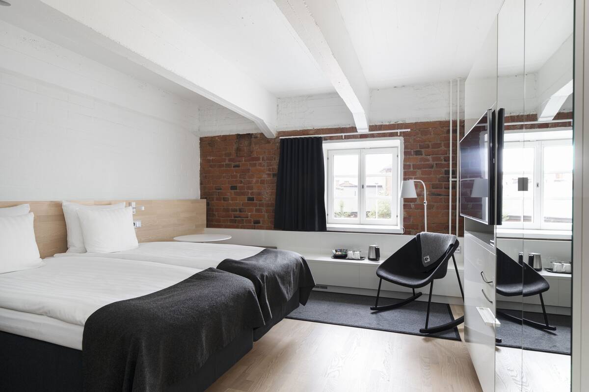 Una habitación de hotel moderna con una cama grande, un escritorio con una silla, un televisor y una pared de ladrillo.