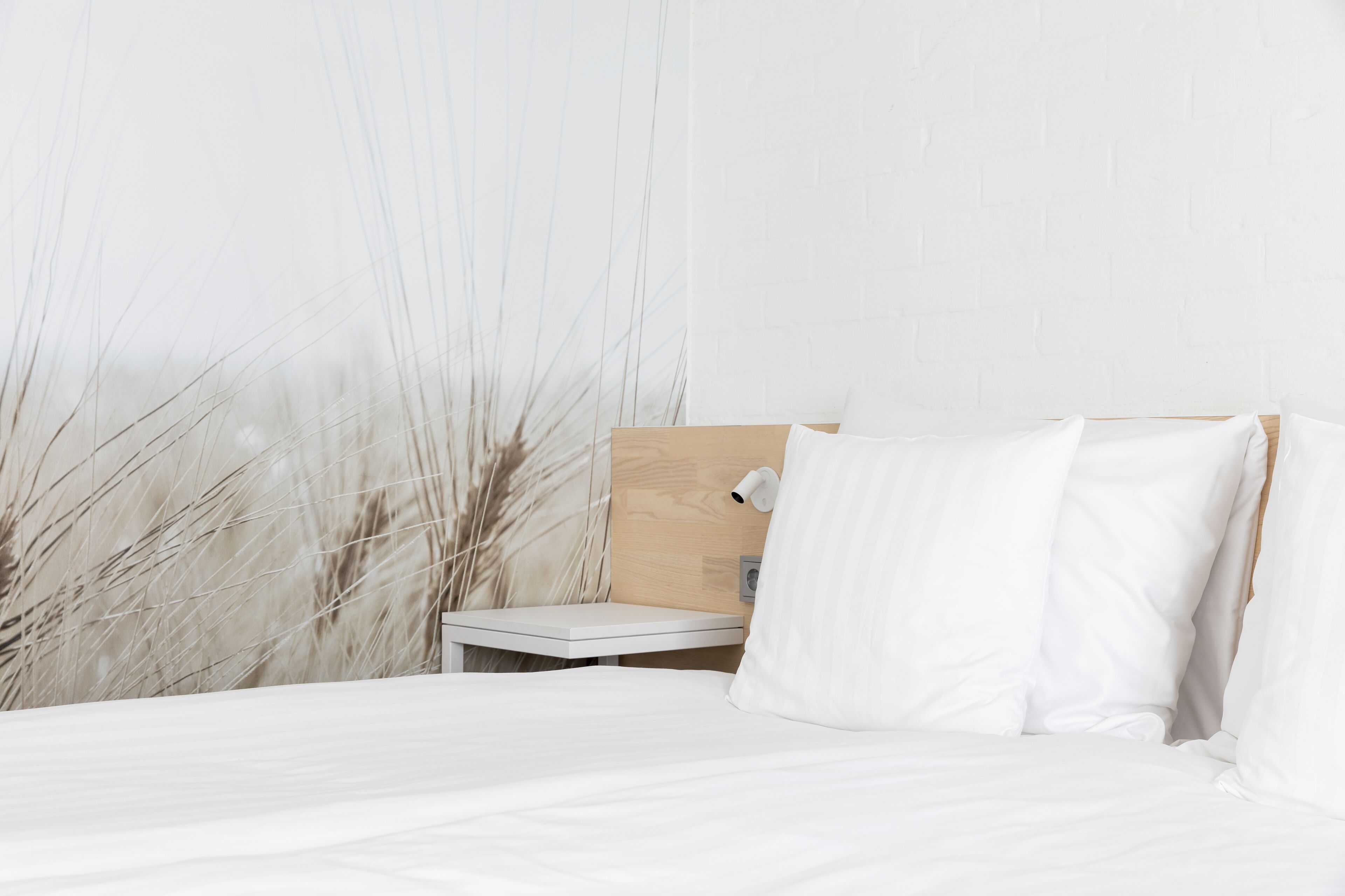A neatly made bed with white linens, a wooden headboard, and a small bedside table with a lamp.
