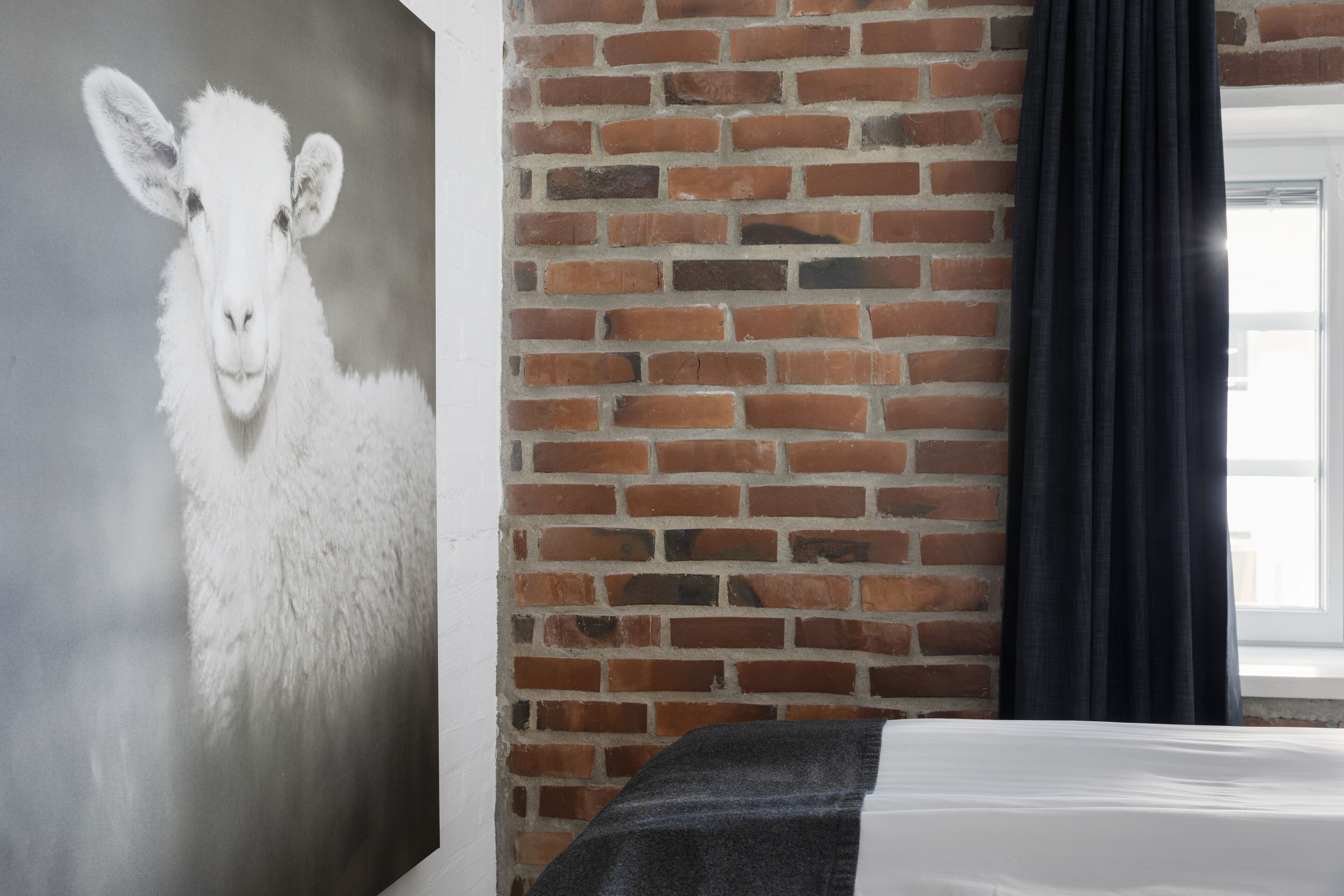 Ein Zimmer mit einer Ziegelwand, einem weißen Bett und einem Schafbild.