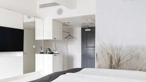 Una habitación de hotel moderna con una cama grande, un televisor de pantalla plana, un armario y un espejo.