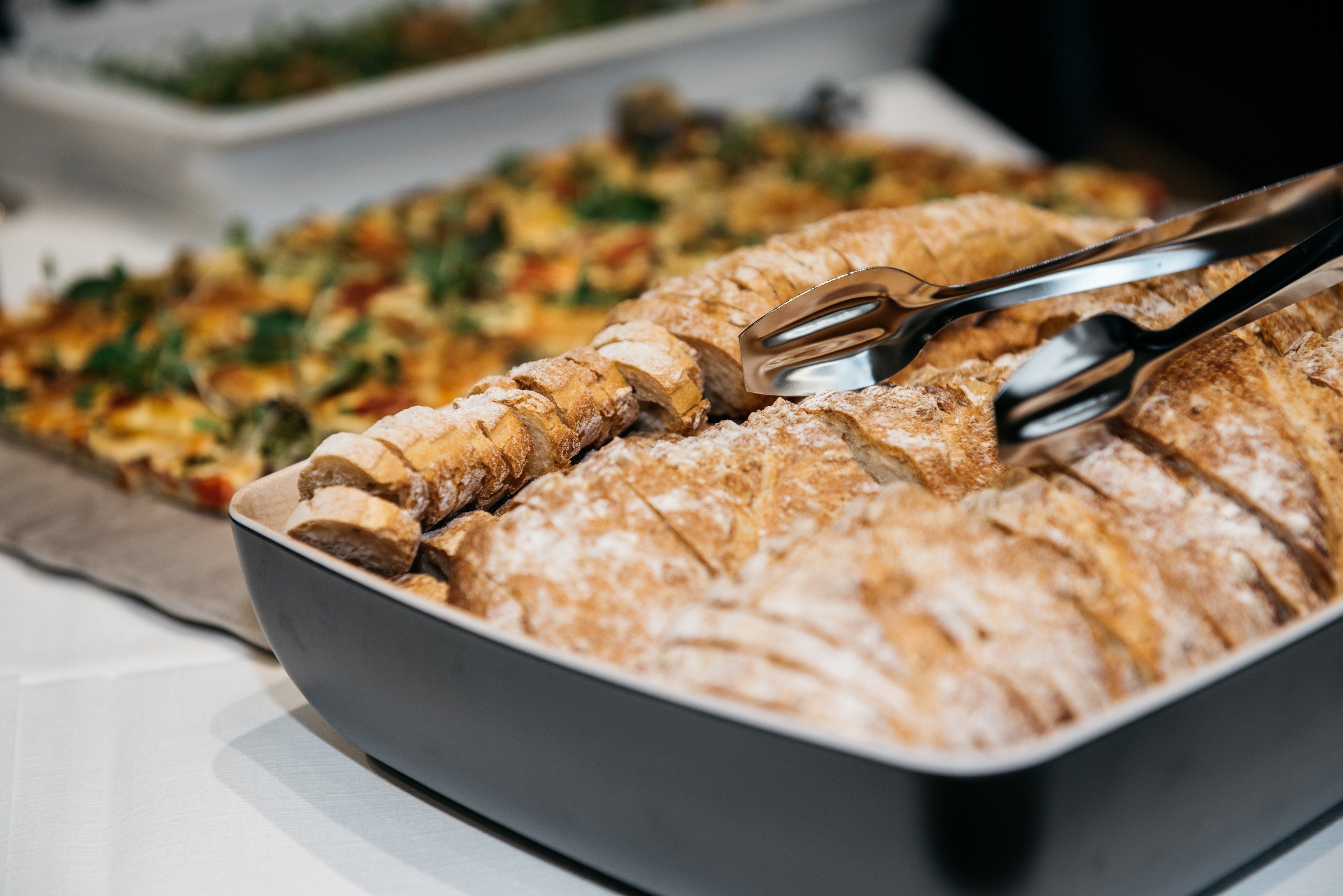 A tray of sliced bread with a dusting of flour, accompanied by a pair of tongs.
