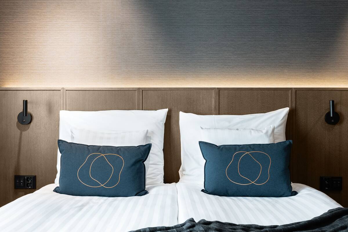 Ein ordentlich bezogenes Bett mit weißen Leinentüchern und zwei Kissen, eines dunkelblau mit schlichtem Muster und eines weiß.