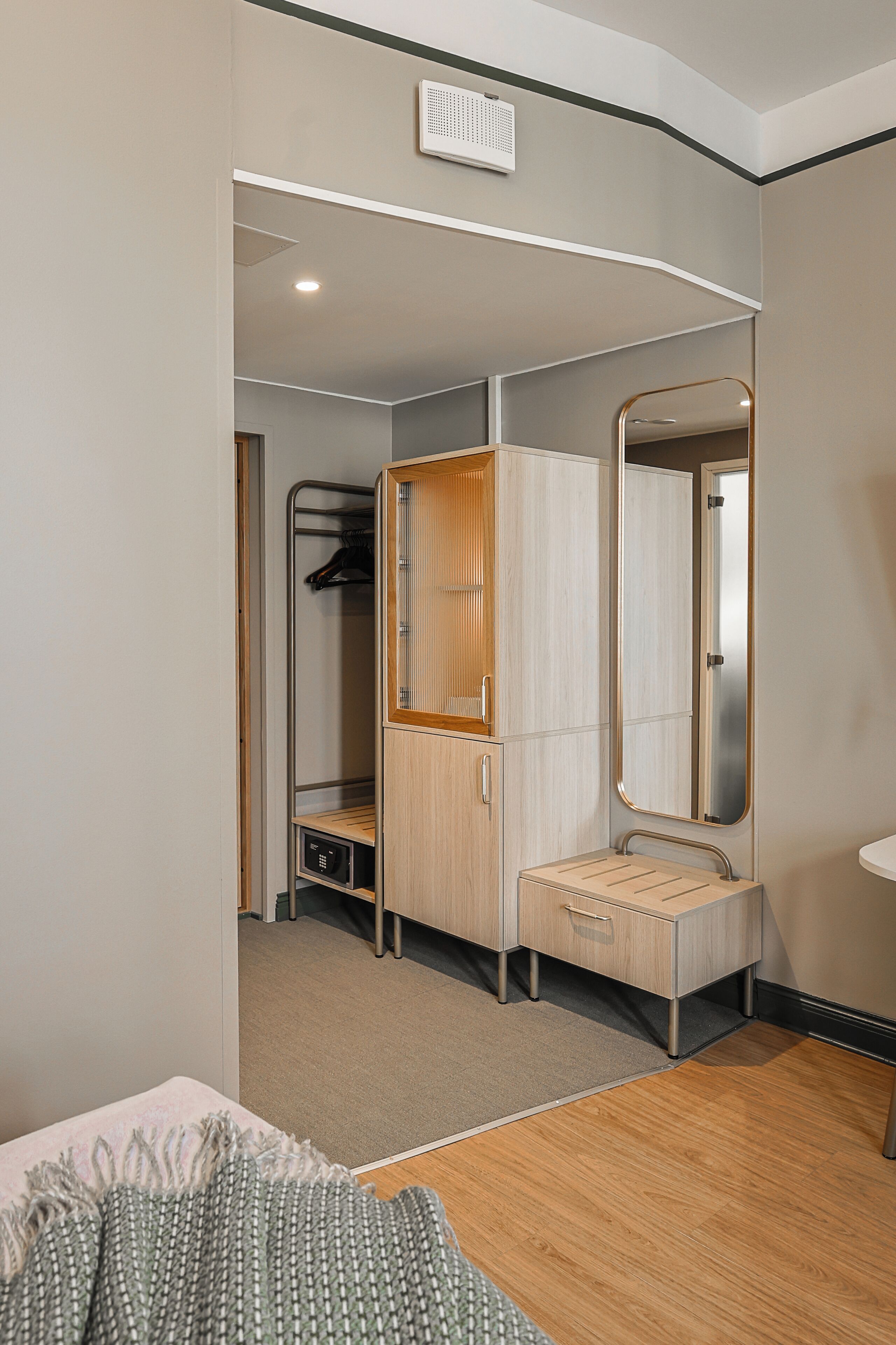 A hotel room with a bed, a wooden wardrobe, a mirror, and a small desk.
