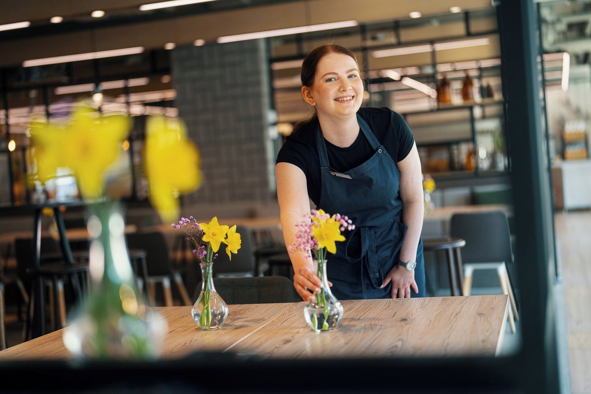 A person arranging flowers on a table in a modern cafe setting.