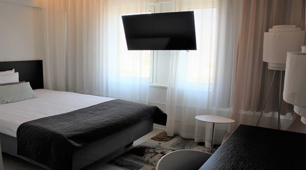 A hotel room with a bed, a flat-screen TV mounted on the wall, a small round table, and a chair.