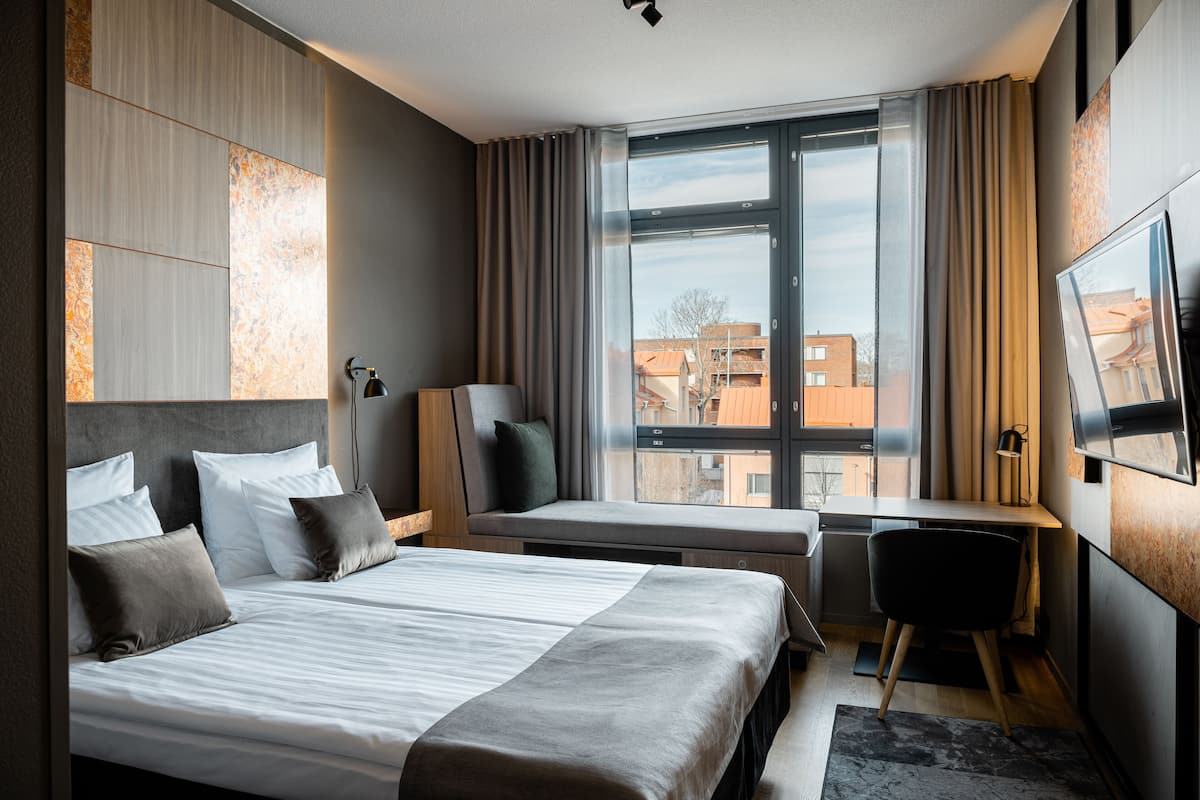 Ein modernes Hotelzimmer mit einem großen Bett, einem Schreibtisch, einem Stuhl und einem Fernseher.