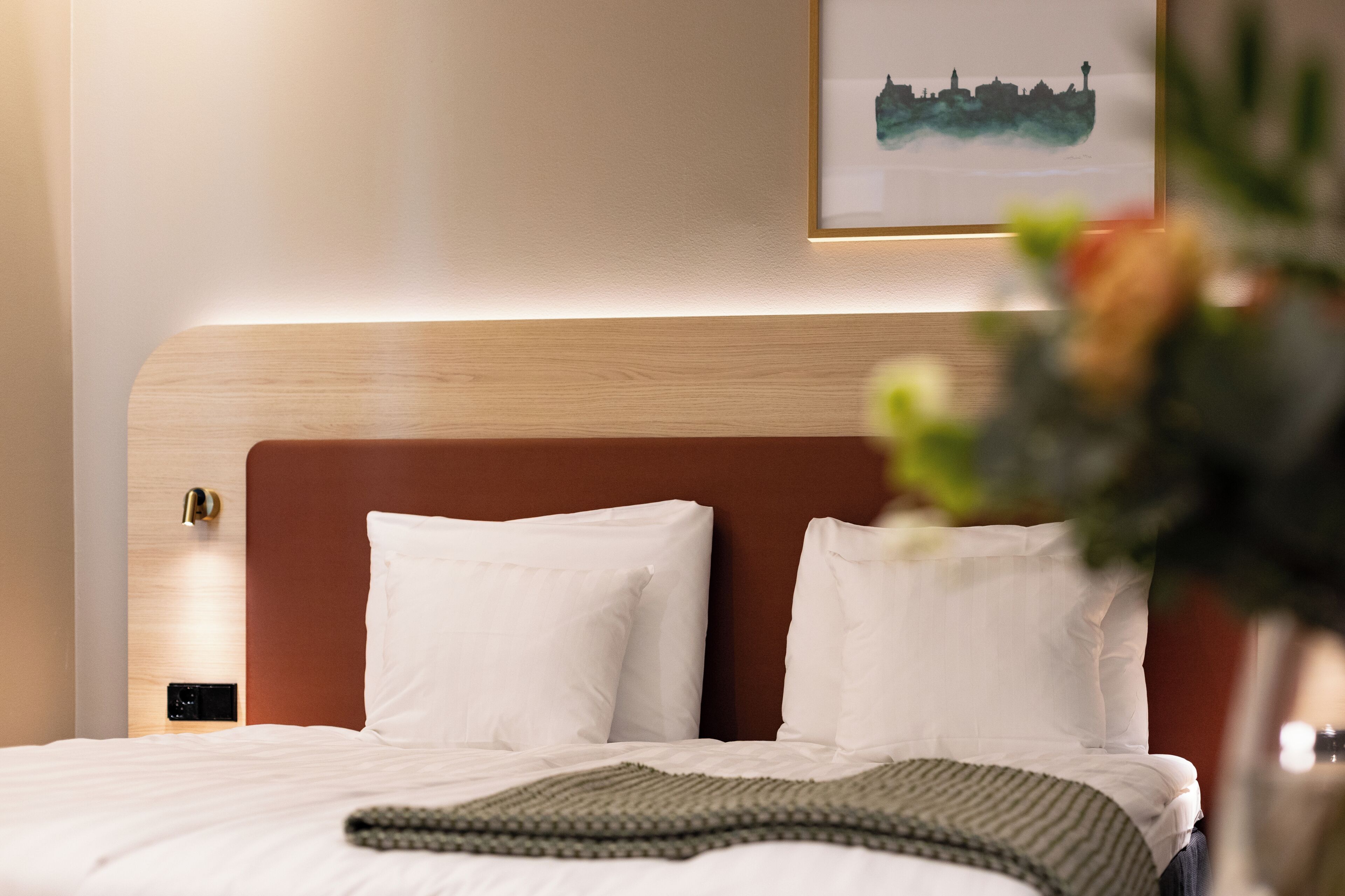 A hotel room with a bed, pillows, a bedside table, and a wall-mounted artwork.