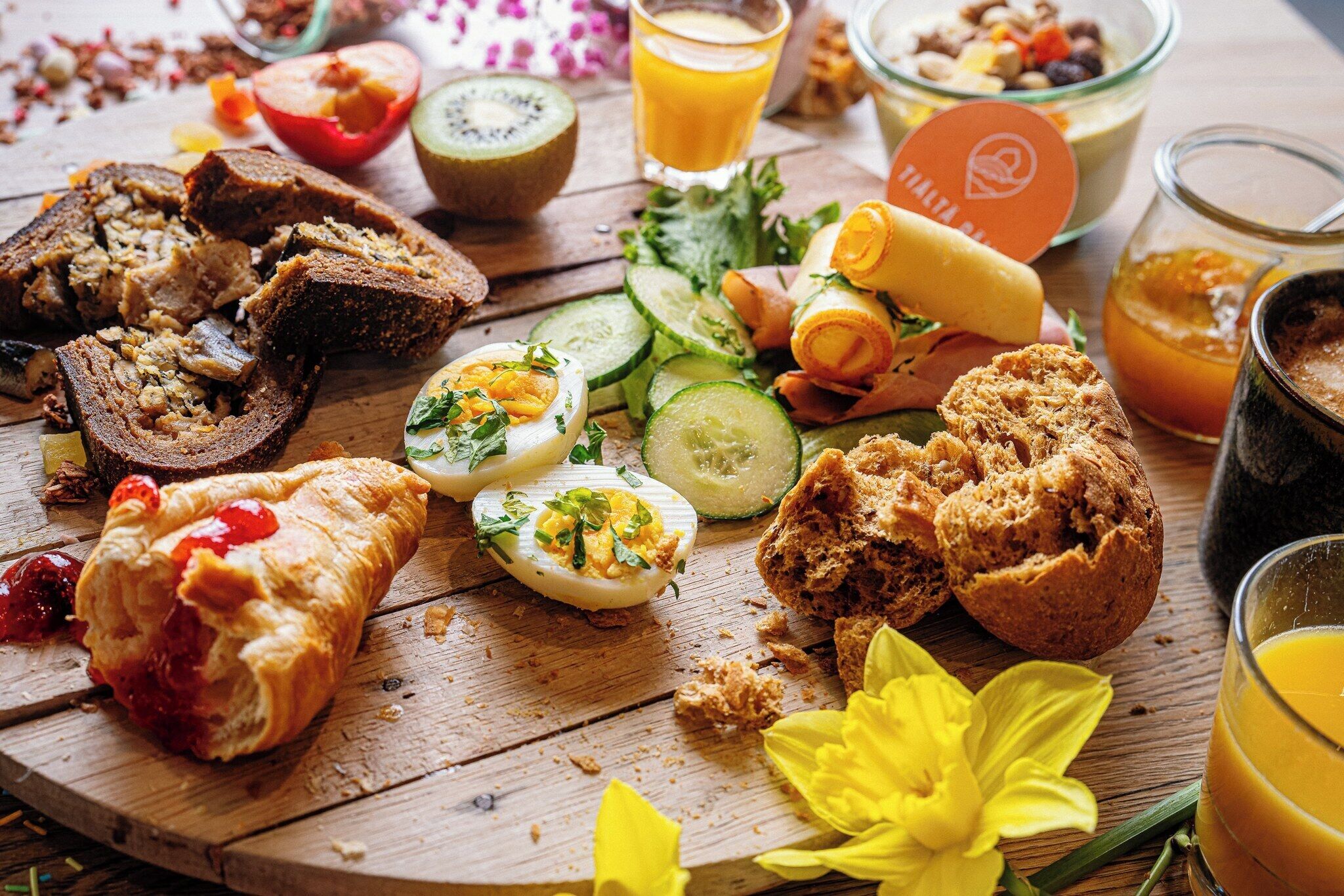 Une table en bois sur laquelle on trouve divers aliments, notamment du pain, des œufs et des légumes.