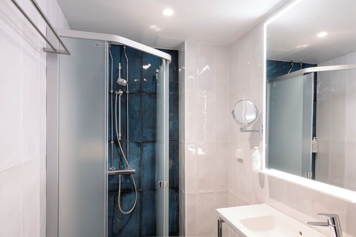 Un baño moderno con ducha de vidrio, lavamanos blanco y un espejo grande.