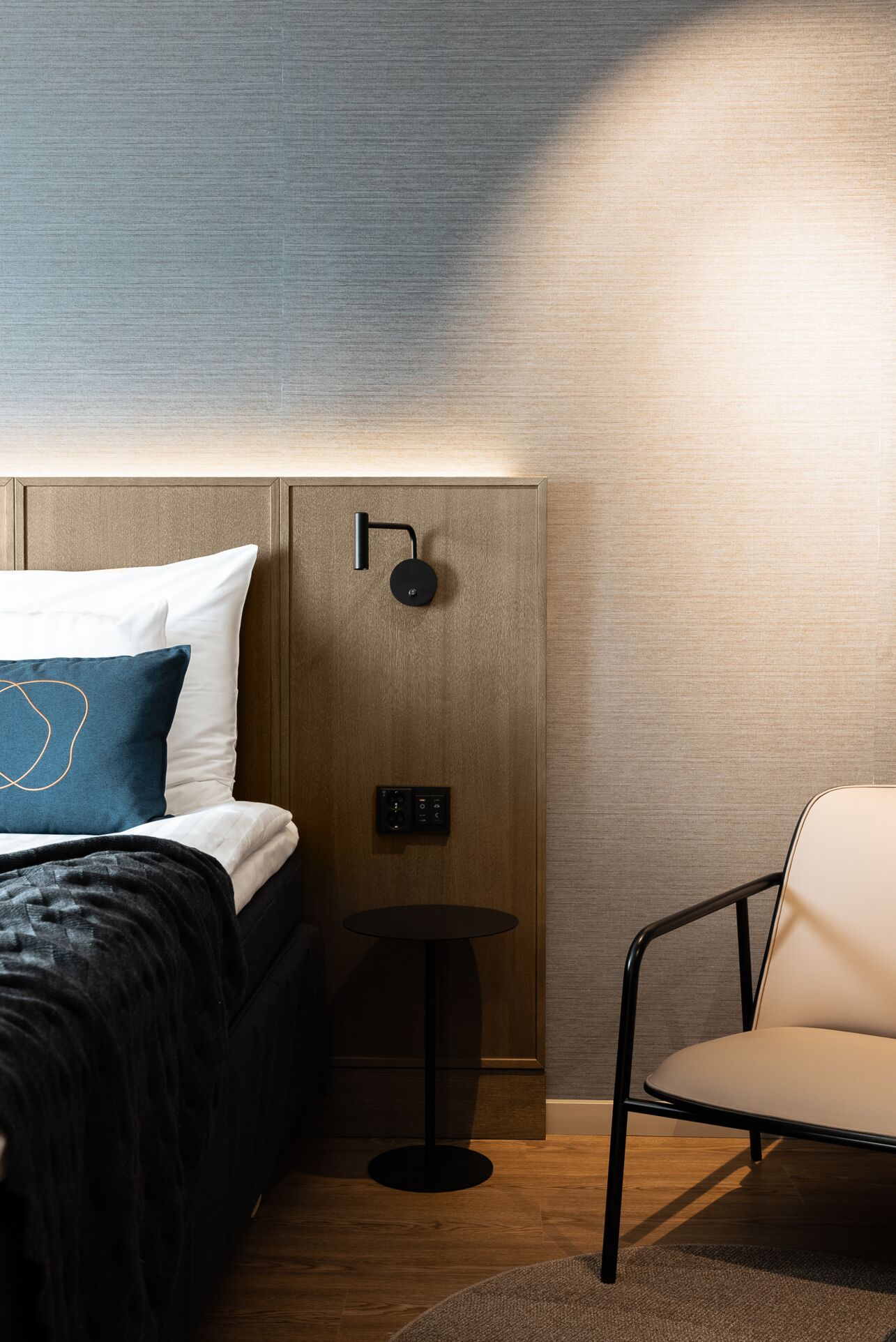 A modern hotel room with a neatly made bed, a small round table, and a chair.
