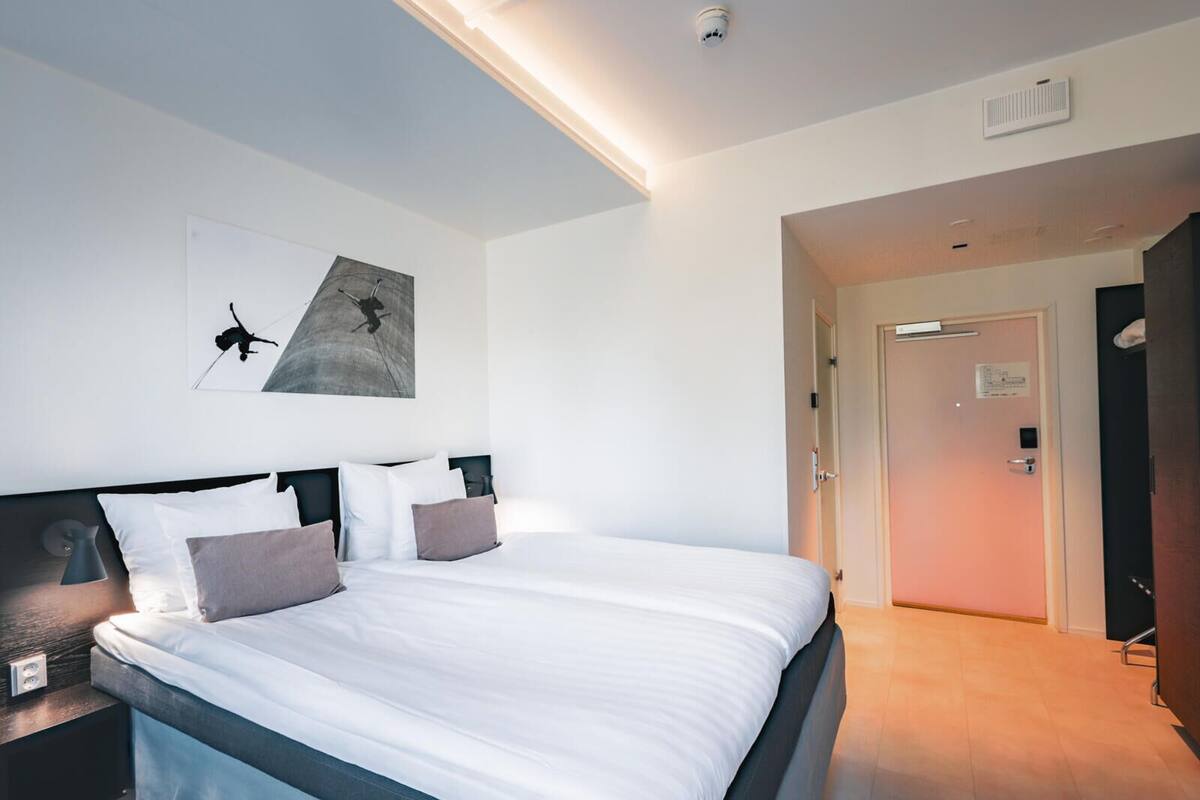 Ein modernes Hotelzimmer mit einem großen Bett, einem Nachttisch, einem Wandbild und einer Tür zu einem weiteren Raum.