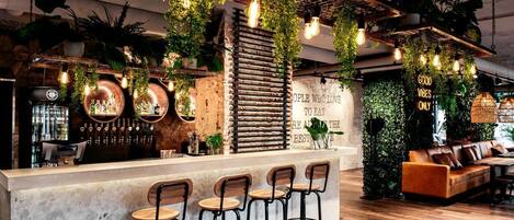 A bar area with a counter, bar stools, and hanging plants. There is a sign on the wall that reads "GOOD VIBES ONLY".