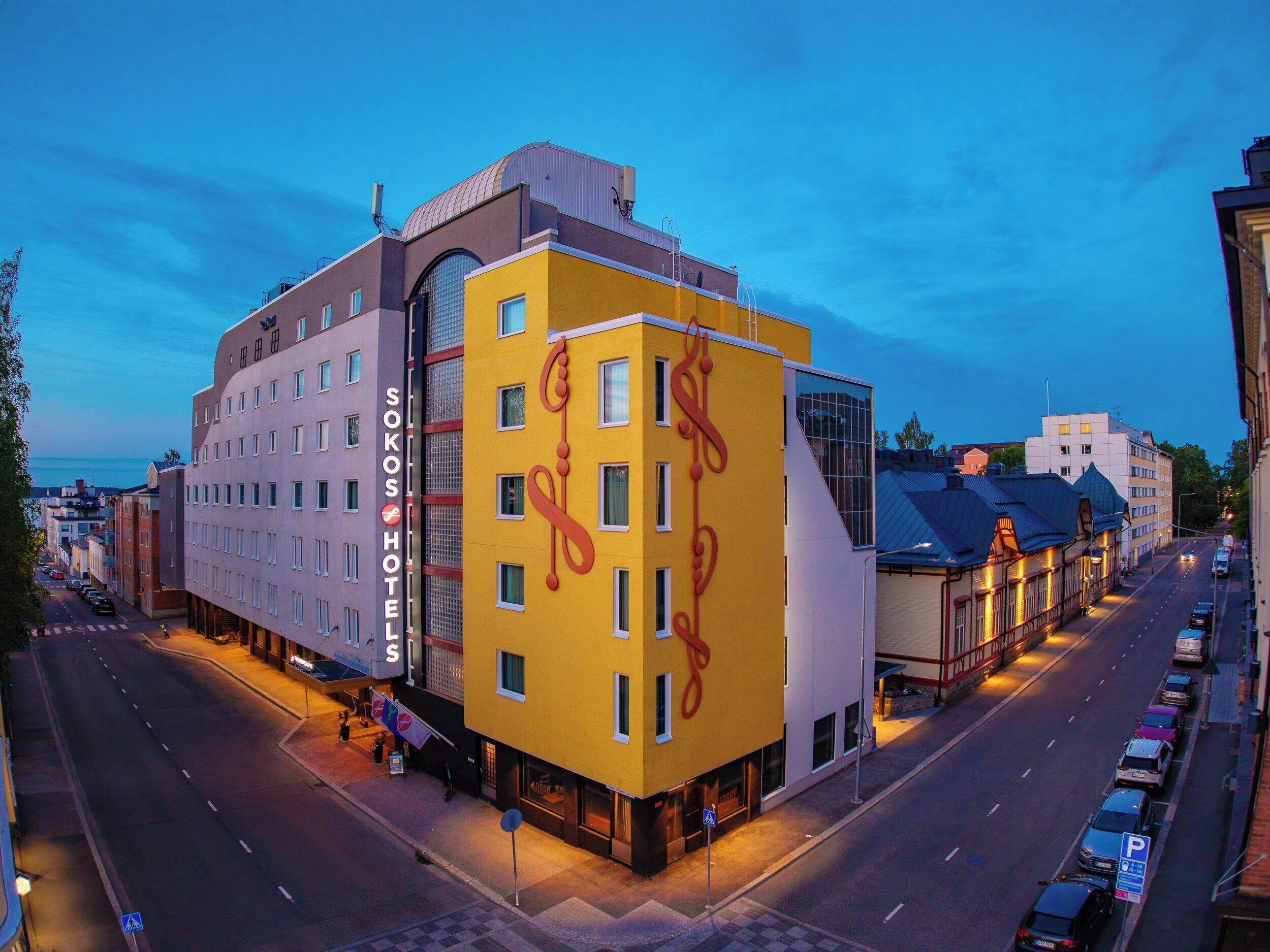 A modern hotel with a distinctive yellow facade and a large window on the ground floor.