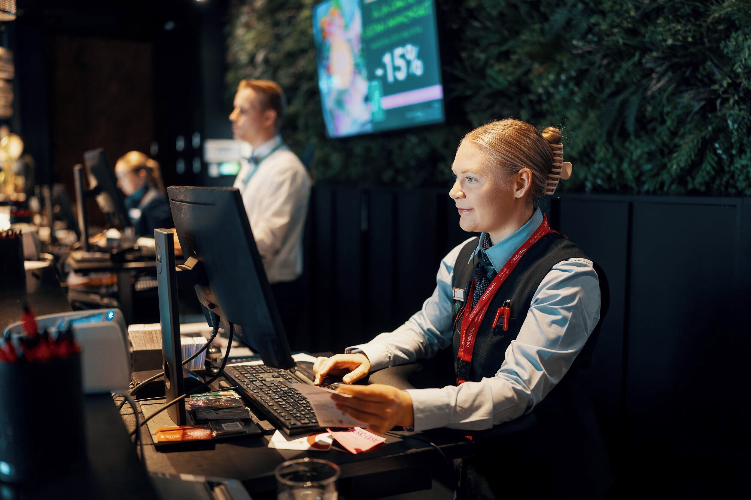 A hotel reception area with a computer desk, a monitor, and a digital screen displaying a percentage.