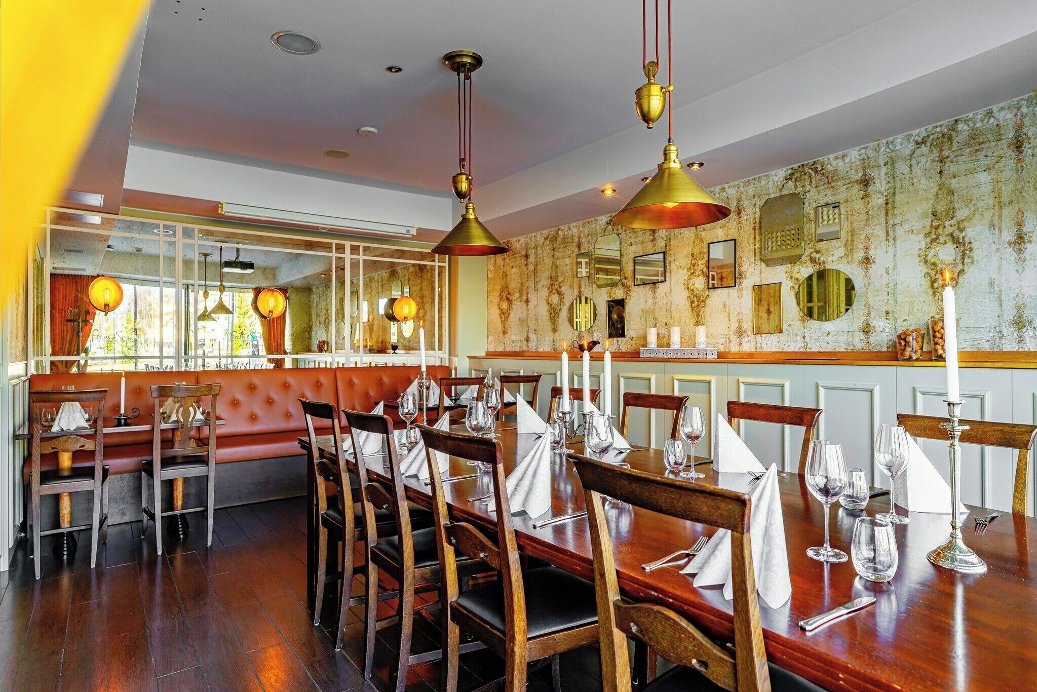A restaurant with wooden tables and chairs, a red cushioned bench, and hanging pendant lights.