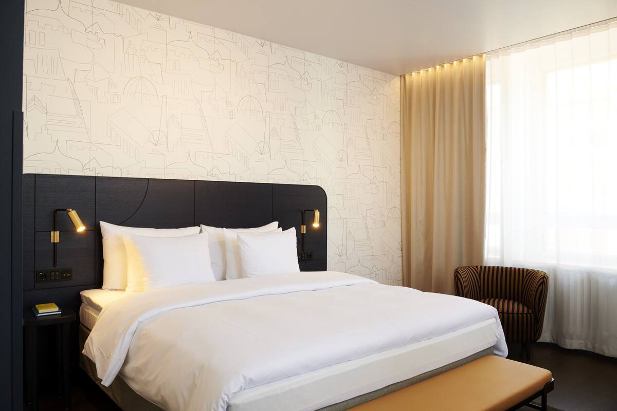 Una habitación de hotel con una cama grande, una mesita de noche, una silla y una ventana con cortinas.